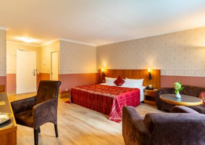 Hotelzimmer mit Doppelbett, roter Tagesdecke und Sitzgelegenheit am Fenster.