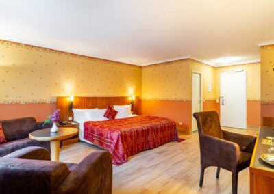 Hotelzimmer mit Doppelbett, Schreibtisch und zwei Sesseln, Tageslicht durch Fenster.