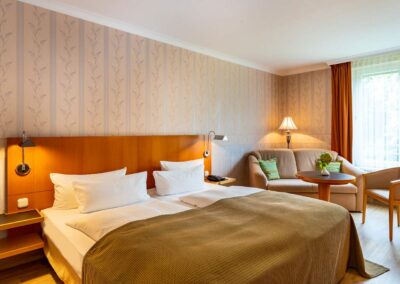 Modern eingerichtetes Zimmer mit großem Doppelbett, Nachttischlampen und Teppichboden.