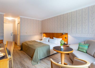 Hotelzimmer mit Doppelbett, kleinem Sofa und heller Wandgestaltung.