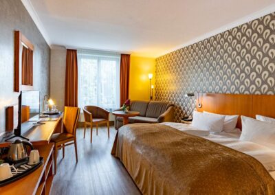 Hotelzimmer mit Doppelbett, Arbeitsbereich und Blick auf eine Fensterfront.