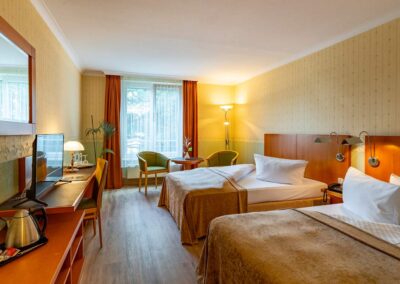 Hotelzimmer mit zwei Doppelbetten, großem Fenster und dekorativen Vorhängen.