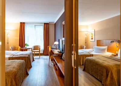 Hotelzimmer mit zwei Doppelbetten, Holzboden und großen Fenstern.