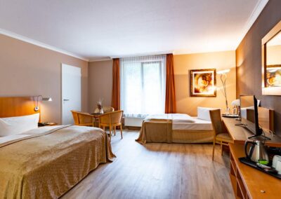 Gemütlich eingerichtetes Hotelzimmer mit Doppelbetten und Holzmöbeln.