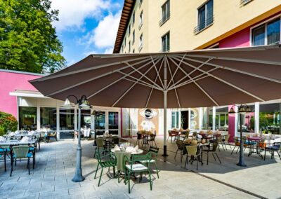 Terrasse mit Tischen, Sonnenschirmen und Blick auf den Hoteleingang.